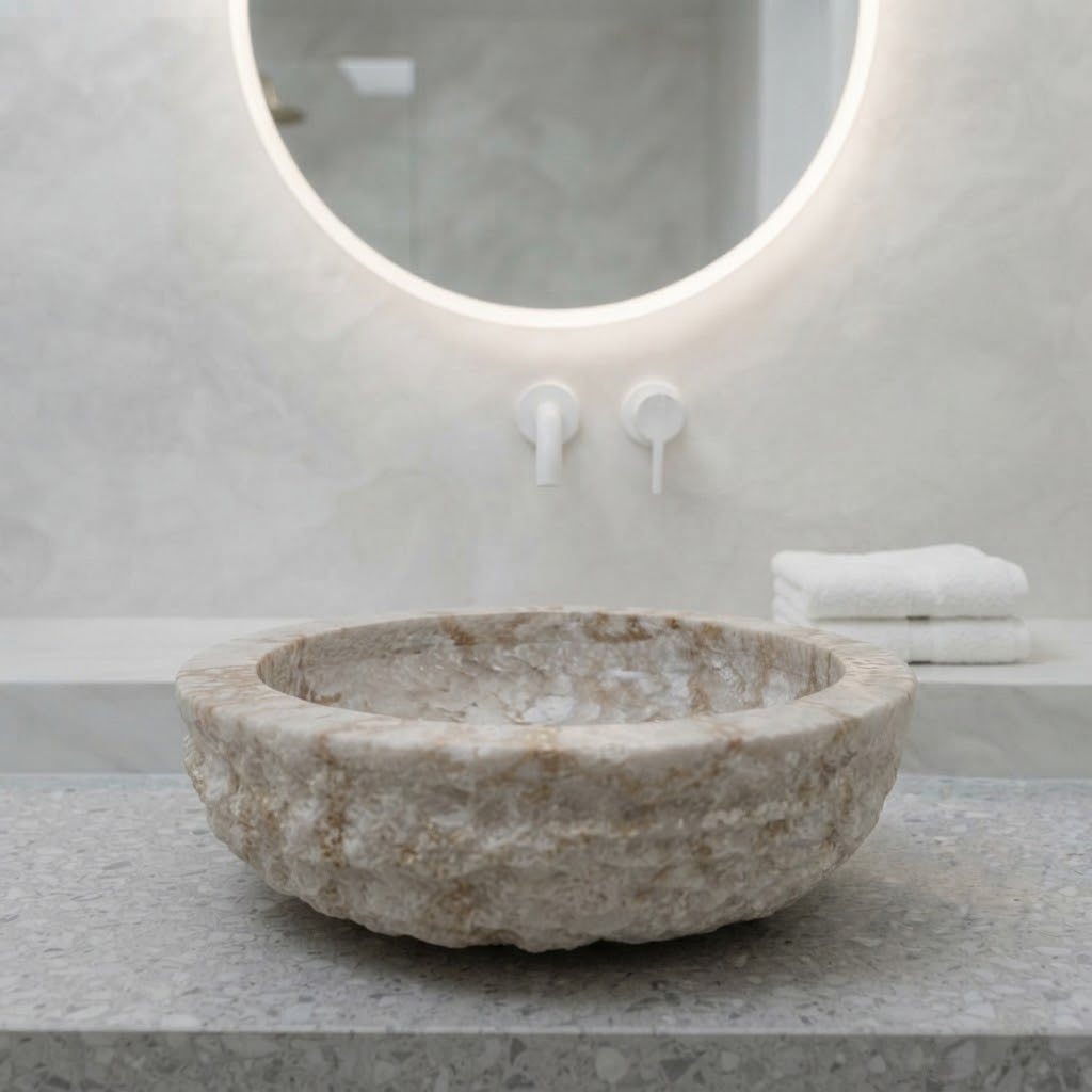 Vasque ronde en marbre naturel crème, brute à l'extérieur, posée sur un plan devant un miroir rond