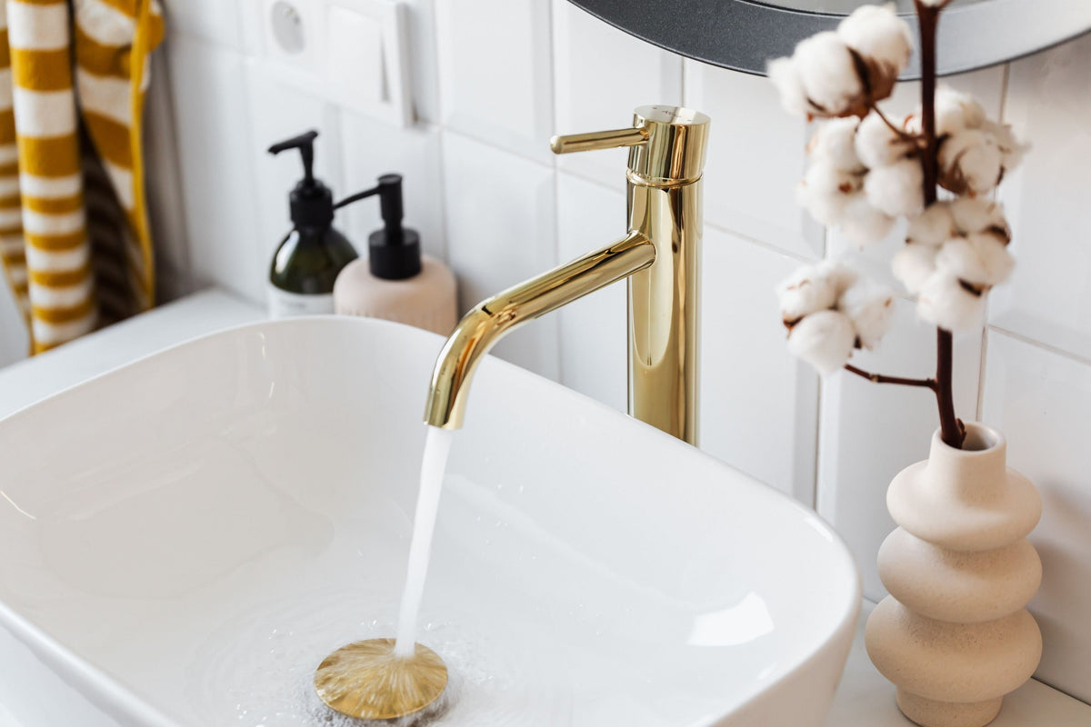 Robinet doré à bec courbe au-dessus d'une vasque à poser blanche, eau qui coule